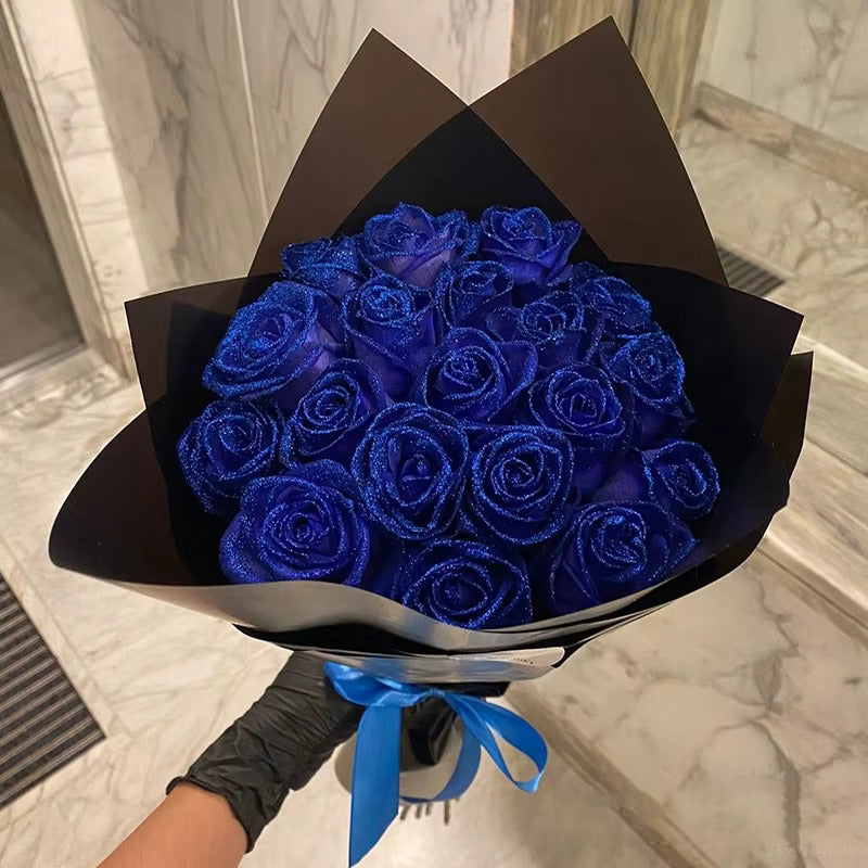 Bouquet of blue roses wrapped in black paper with a blue ribbon, held against a marble floor background.